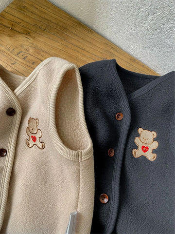 Close-up of the embroidered teddy bear holding a red heart on the Apricot and Navy fleece vests